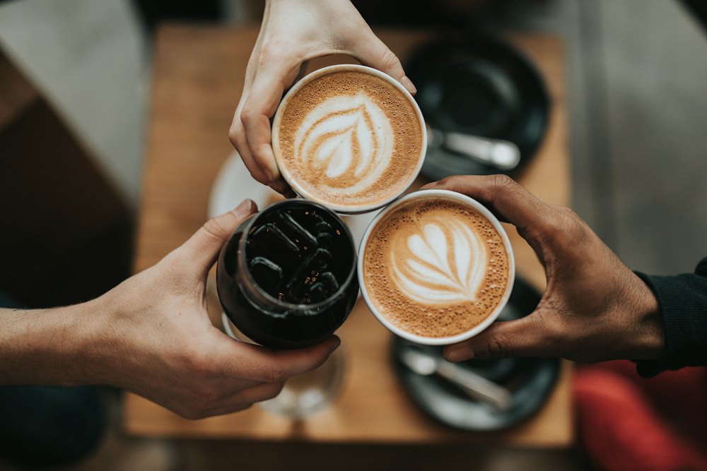 Tiga gelas kopi disentuhkan bersama di atas meja kayu