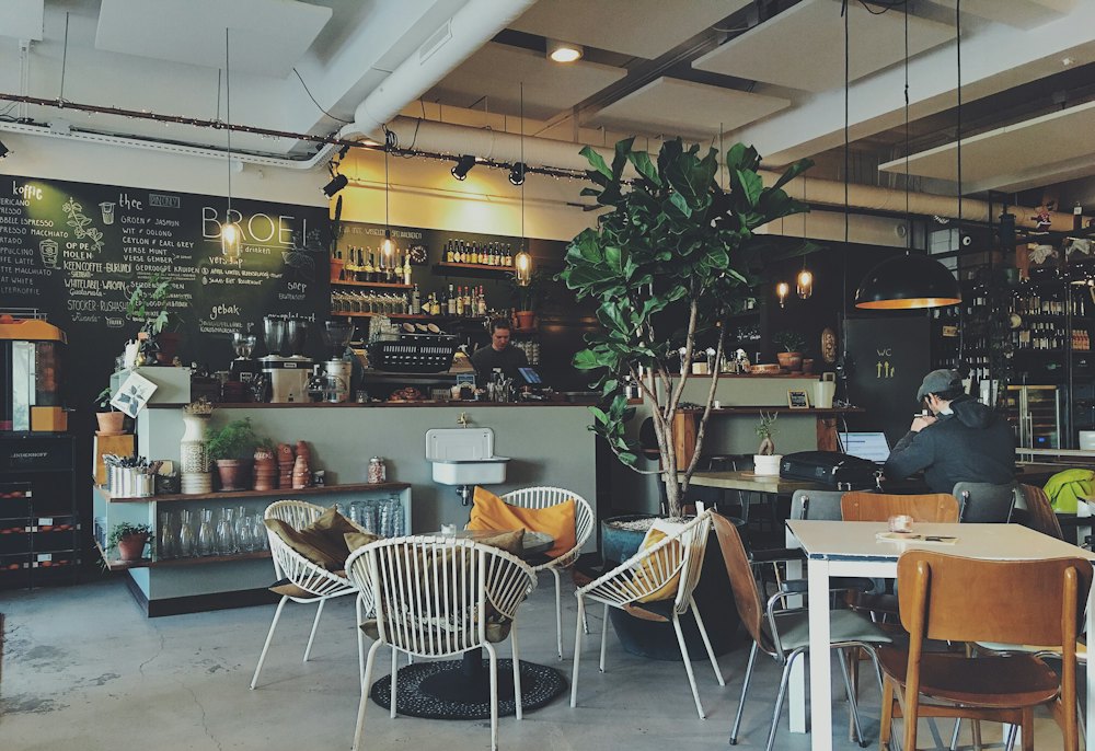 Ruang warung dengan meja, tanaman besar, dan meja bar